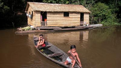 Children in a canoe beside their house made of Babassu straw (Orbygnia phalerata) in the Amazon Upland Rainforest